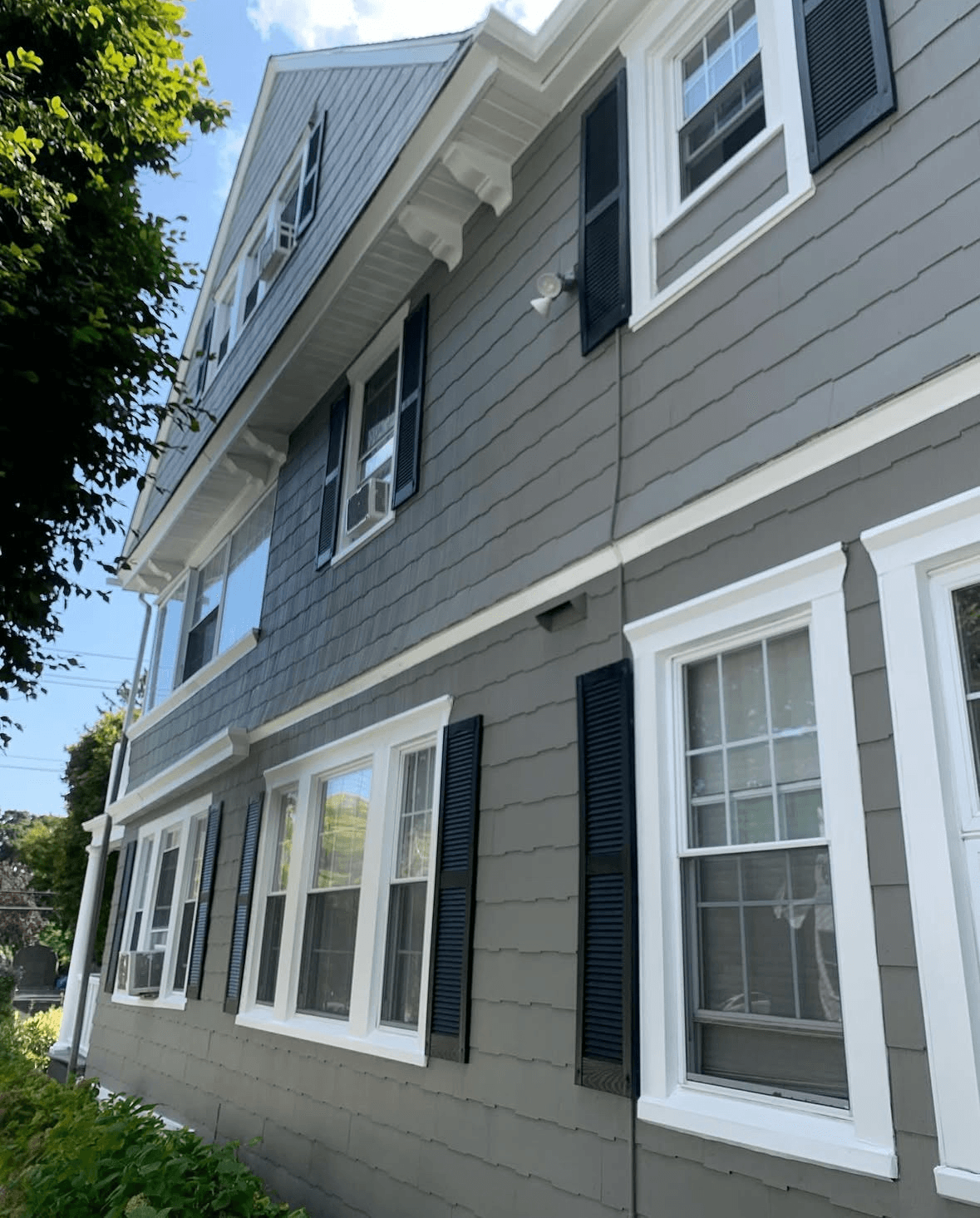 Upward side angle of the renovated colonial — crisp gray shingle siding, white trim, black louvered shutters