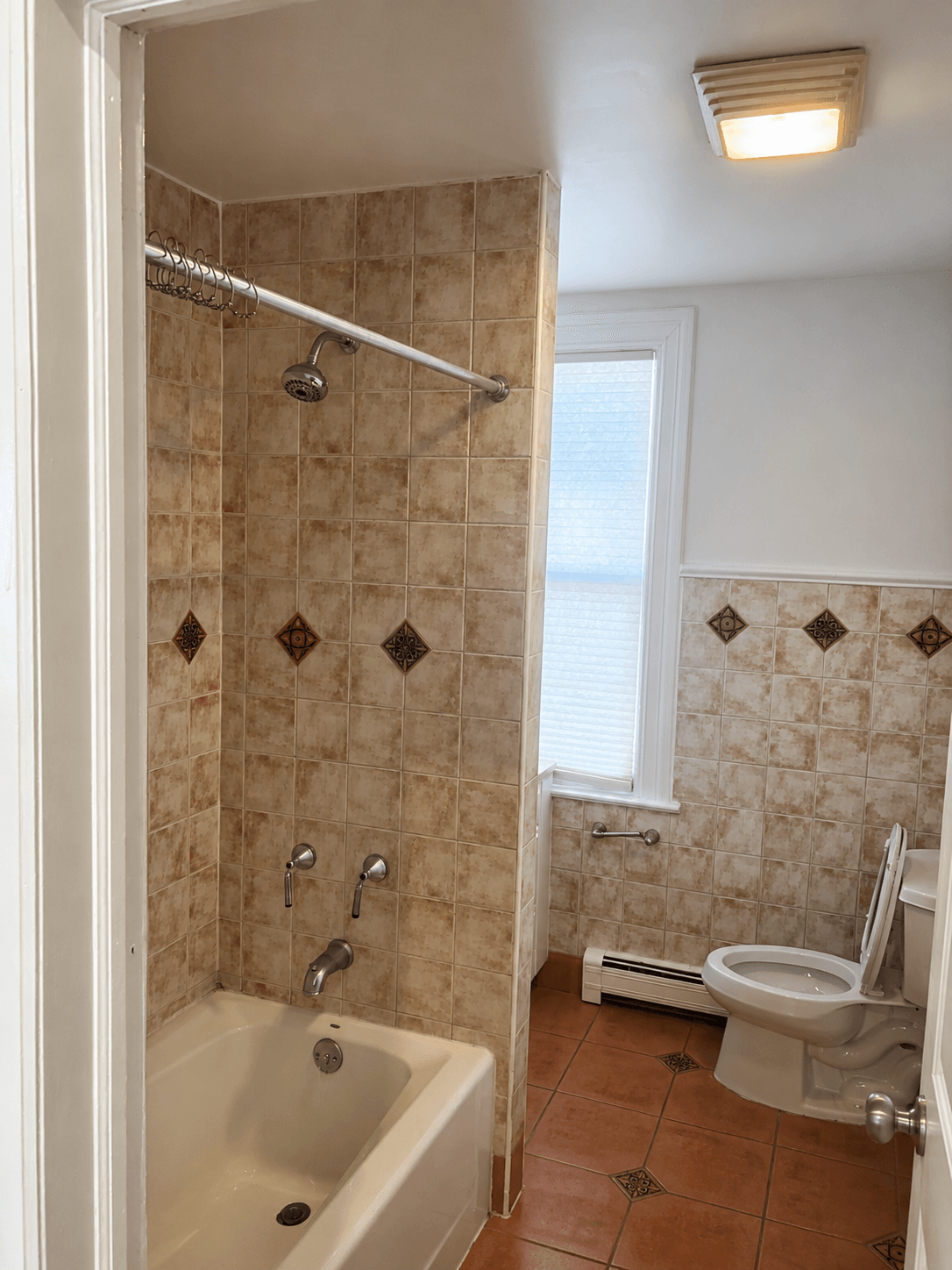 Dated hall bathroom before renovation — beige tile walls with diamond accents, terracotta floor, and old tub surround
